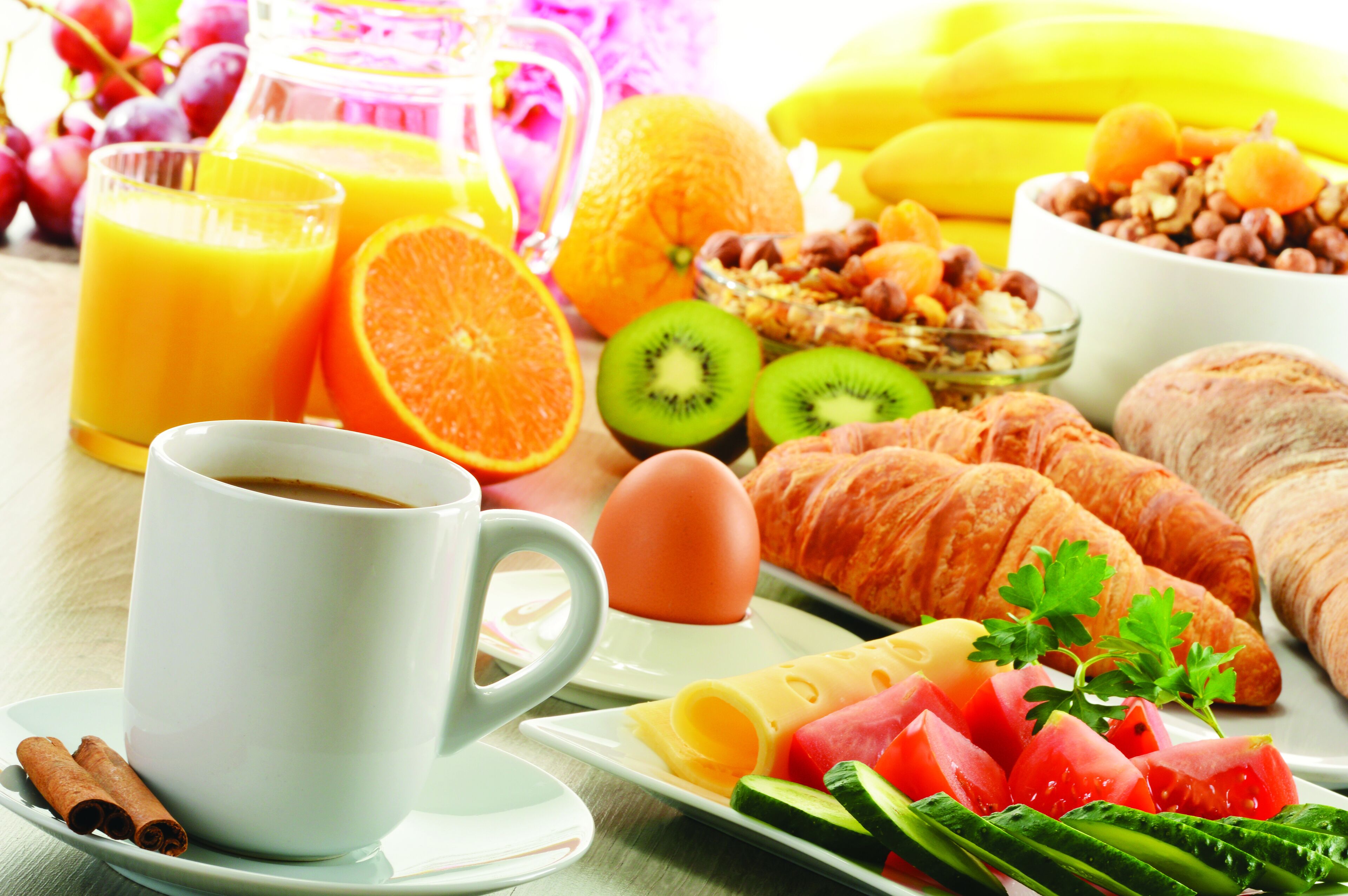 A breakfast setting with a cup of coffee, orange juice, croissants, eggs, and fresh fruits.