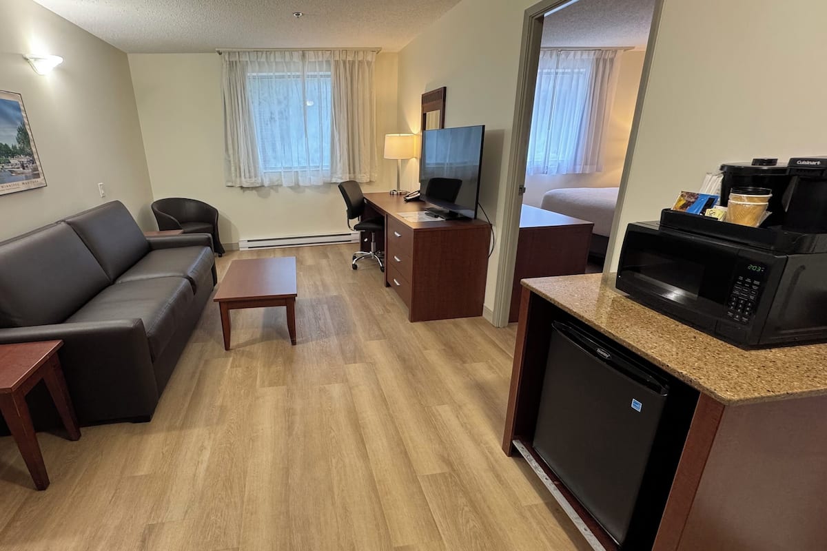 A compact hotel room with a sofa, a small desk, a television, a microwave, and a coffee machine.