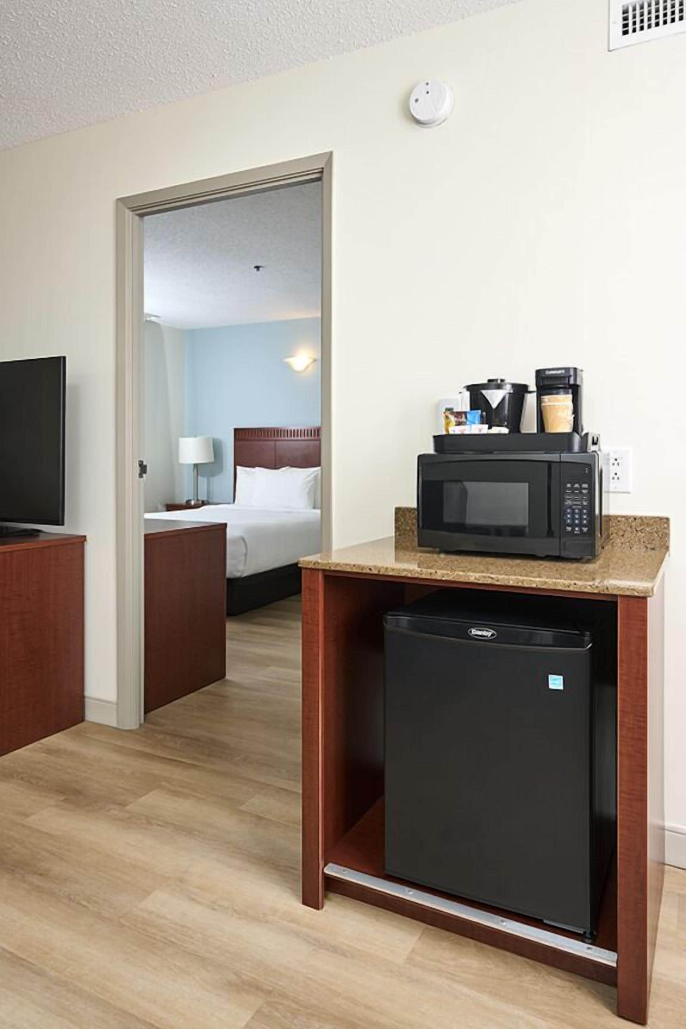 Una habitación de hotel con kitchenette, una cama, un televisor y un microondas.