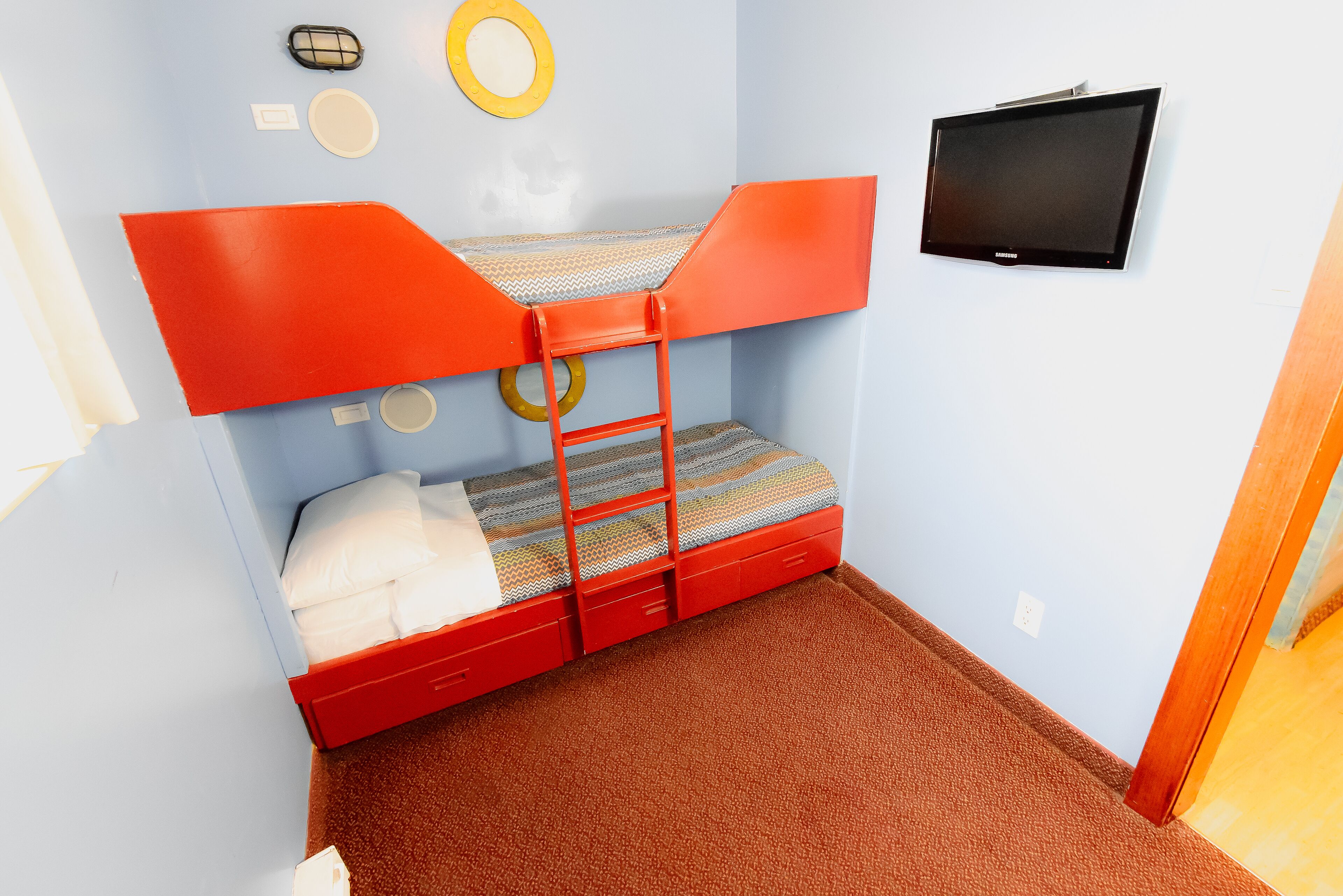 Una cama individual con una televisión montada en la pared, una alfombra pequeña y una pared azul claro con un adorno circular.