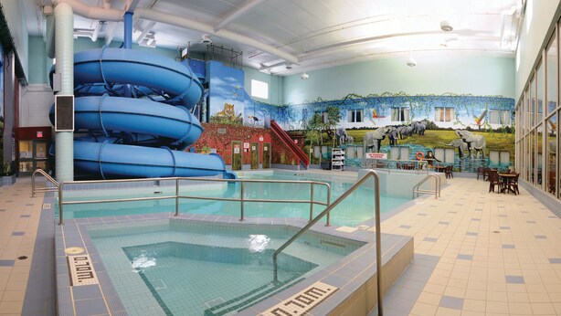 An indoor swimming pool with a water slide, a mural, and a seating area.