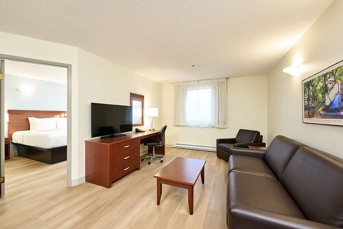 A hotel room with a bed, a desk with a computer, a TV, a sofa, and a painting on the wall.