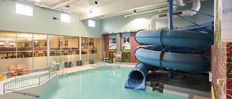 Una piscina interior con tobogán de agua, zona de estar y vistas a la piscina a través de paredes de vidrio.