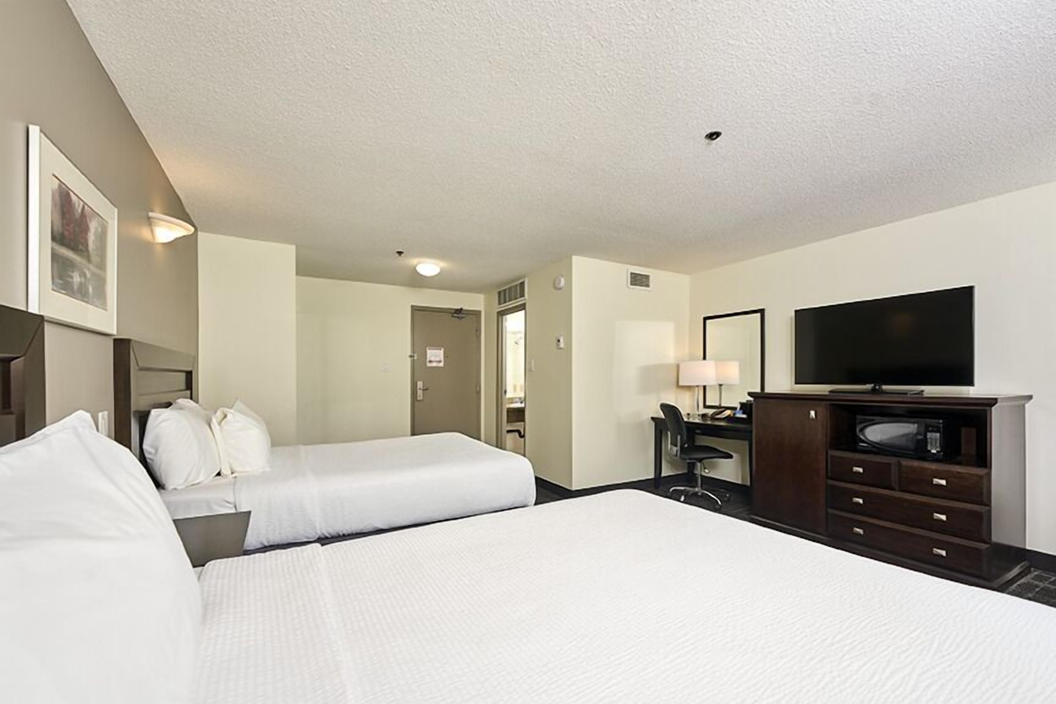 A hotel room with two beds, a desk, a television, and a mirror.