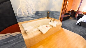 A room with a large bathtub, a wooden floor, a wall mural of an iceberg, and a desk with a chair.