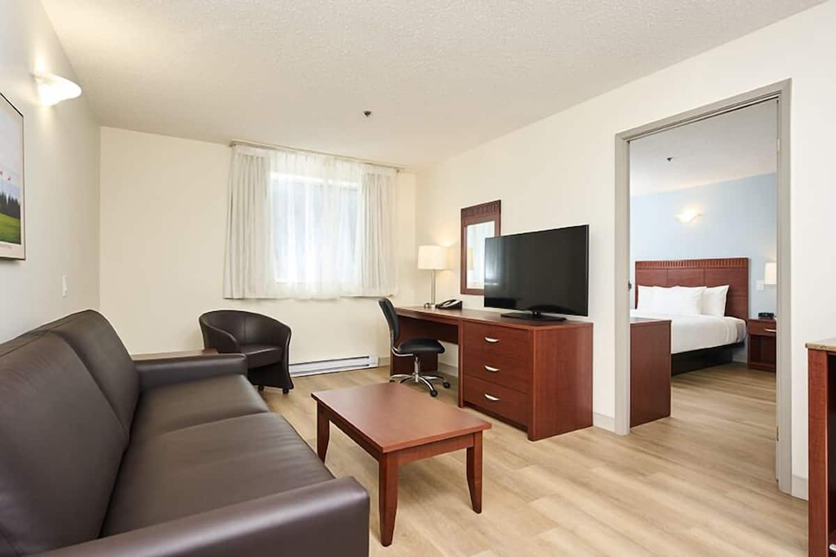 A hotel room with a leather sofa, a wooden desk, a television, a bed with white bedding, and a large mirror.