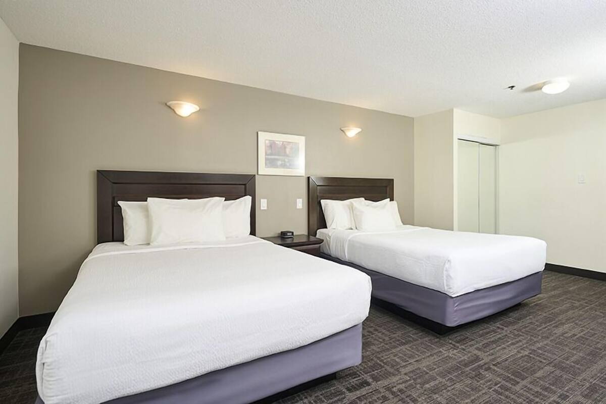 A hotel room with two beds, a small table, and a picture on the wall.