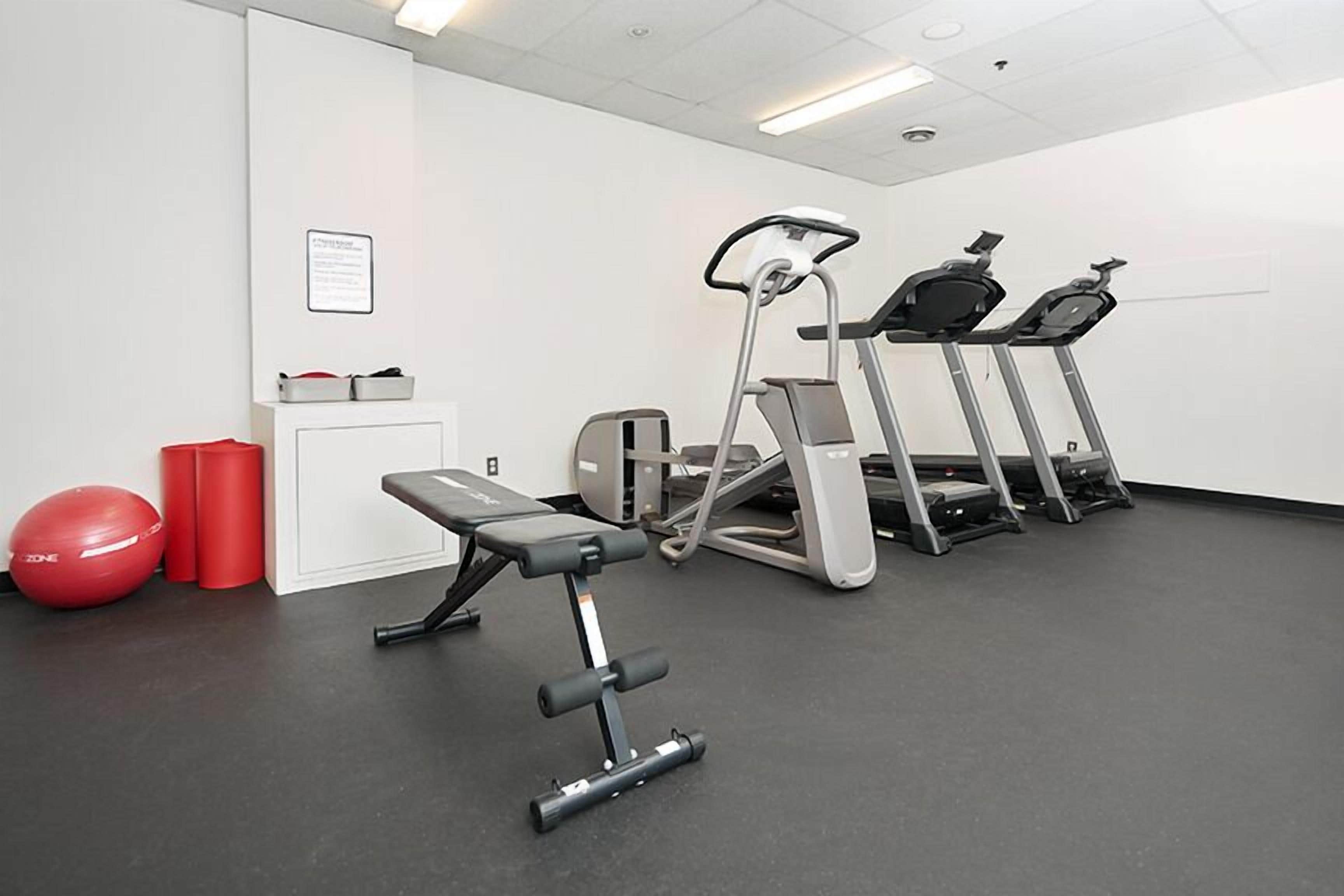 Une salle de sport équipée de tapis de course, d’un banc et de ballons d’exercice rouges.