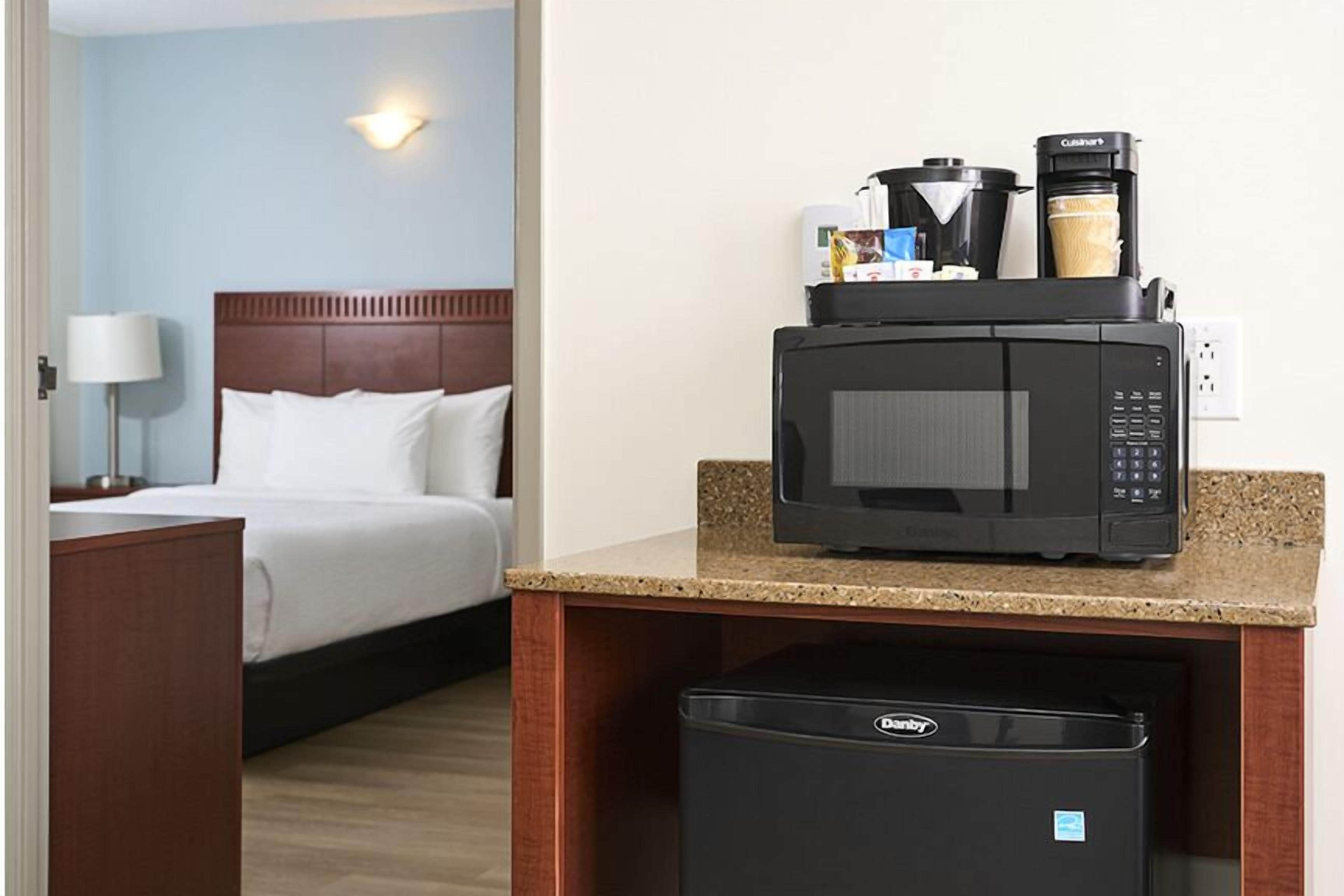 A hotel room with a bed, a desk with a microwave, a coffee maker, and a mini fridge.