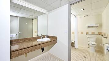 A bathroom with a sink, mirror, toilet, and shower area.