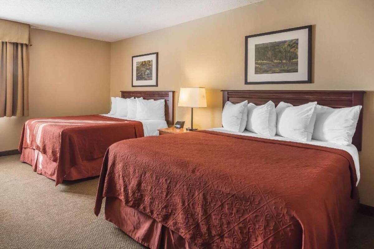 A hotel room with two beds, a nightstand, a lamp, and two framed pictures on the wall.