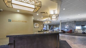 A reception area with a reception desk, a stone accent wall, and a seating area with chairs and a potted plant. - Quality Hotel & Conference Centre Fort McMurray (Fort McMurray)