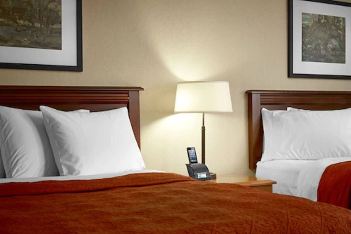 A hotel room with two beds, a nightstand with a lamp, and artwork on the walls.