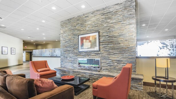 A lobby with a stone wall, two orange armchairs, a brown sofa, a coffee table, and a framed picture. - Quality Hotel & Conference Centre Fort McMurray (Fort McMurray)