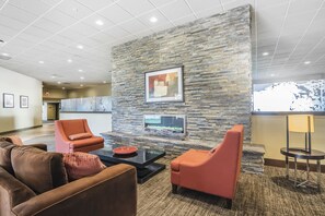 A lobby with a stone wall, two orange armchairs, a brown sofa, a coffee table, and a framed picture. - Quality Hotel & Conference Centre Fort McMurray (Fort McMurray)