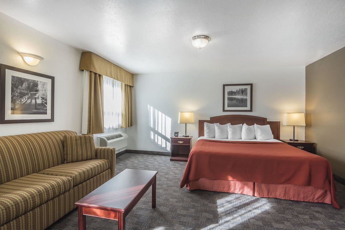 A hotel room with a bed, a sofa, a table, and two bedside lamps.