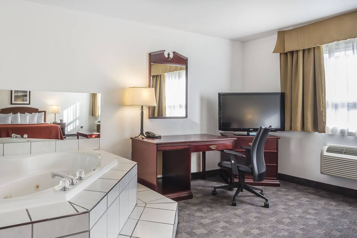 A hotel room with a large bathtub, a desk with a chair, a television, and a mirror.