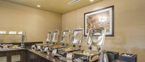 A buffet area with various food stations, including a bowl of maple syrup, and a framed artwork on the wall.