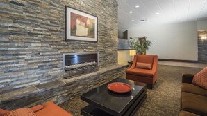 A lobby with a stone wall, a fireplace, orange sofas, and a framed picture. - Quality Hotel & Conference Centre Fort McMurray (Fort McMurray)