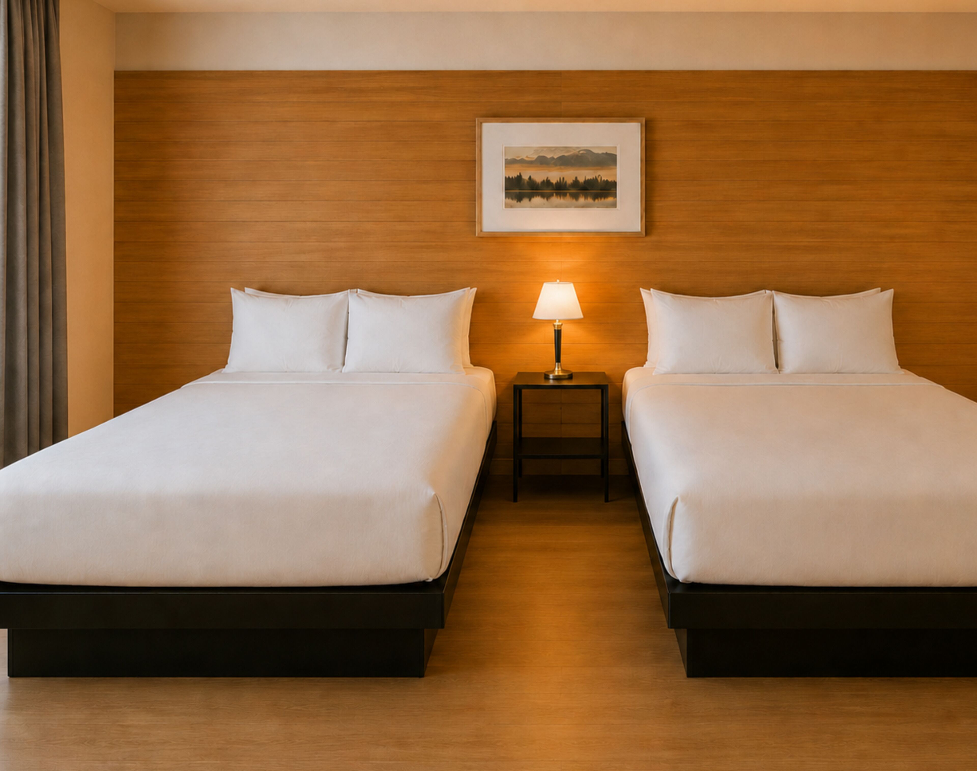 A hotel room with two beds, a nightstand with a lamp, and a framed picture on the wall.