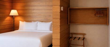 Una habitación con una cama, una lámpara, un banco de madera y una estantería en la pared.