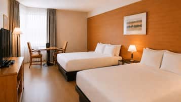 Een hotelkamer met twee bedden, een bureau, een stoel, een televisie en een lamp.