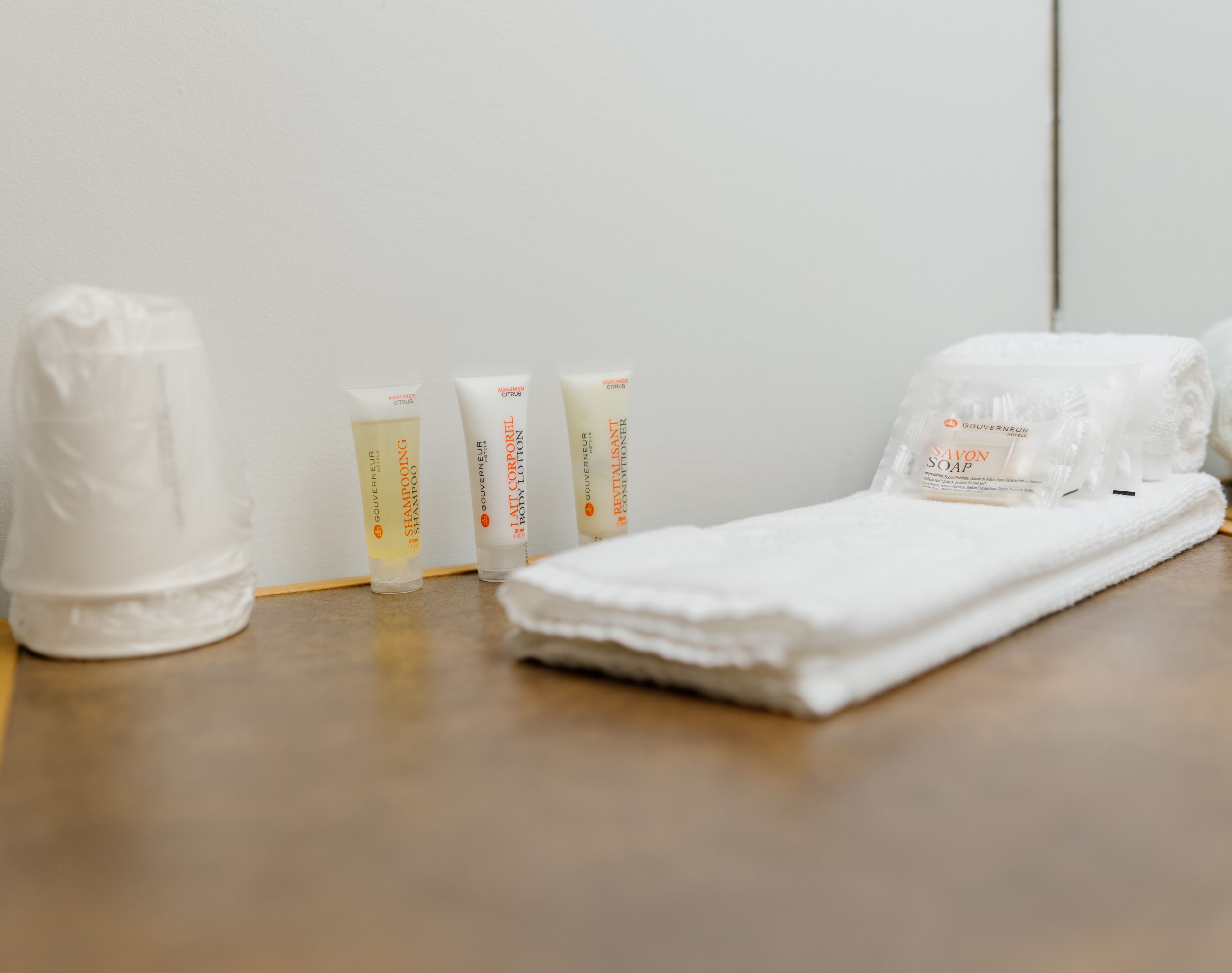 A bathroom with a white towel, a white bathrobe, and three toiletries on a wooden surface.
