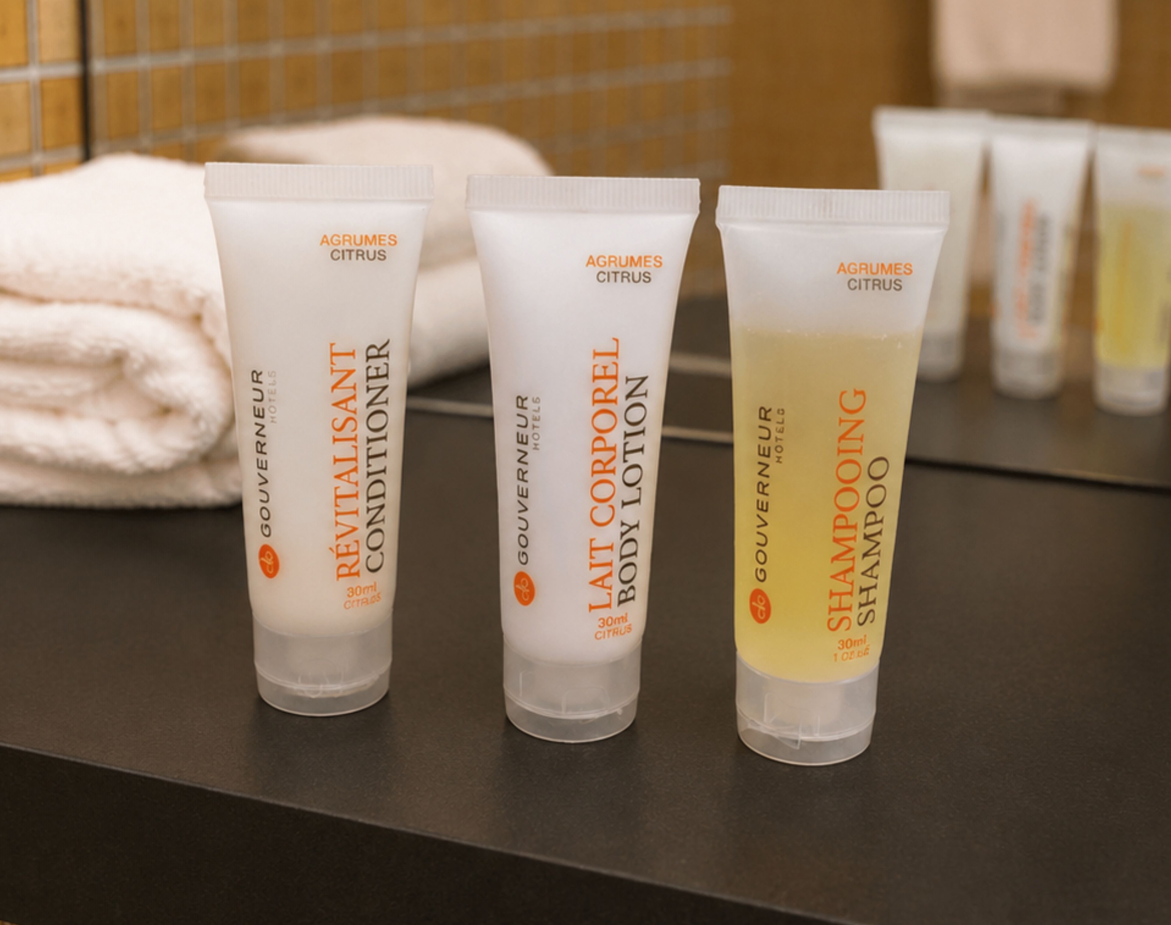 Three toiletry bottles labeled AGRUMES CITRUS on a bathroom counter.