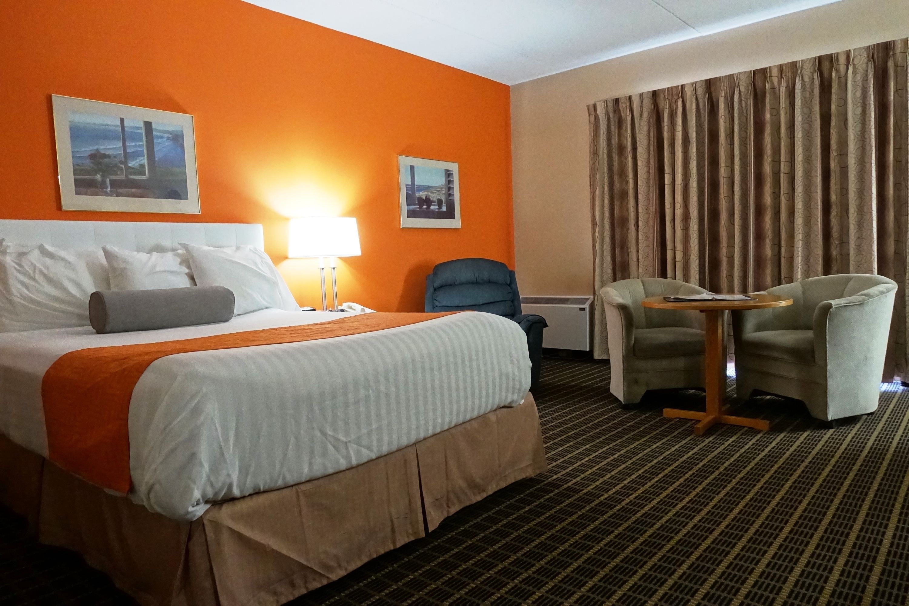 Habitación de hotel con una cama grande, un escritorio con dos sillas, una lámpara y dos cuadros en la pared.