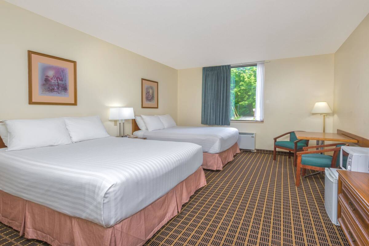 Een hotelkamer met twee bedden, een bureau, een stoel, een raam met gordijnen en een muur met ingelijste foto's.