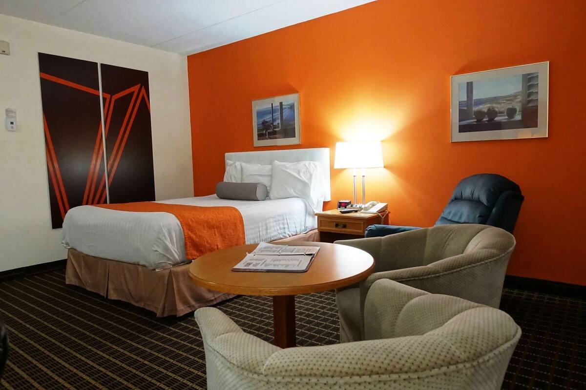 Een hotelkamer met een bed, een bureau, een stoel en twee foto's in lijsten aan de muur.