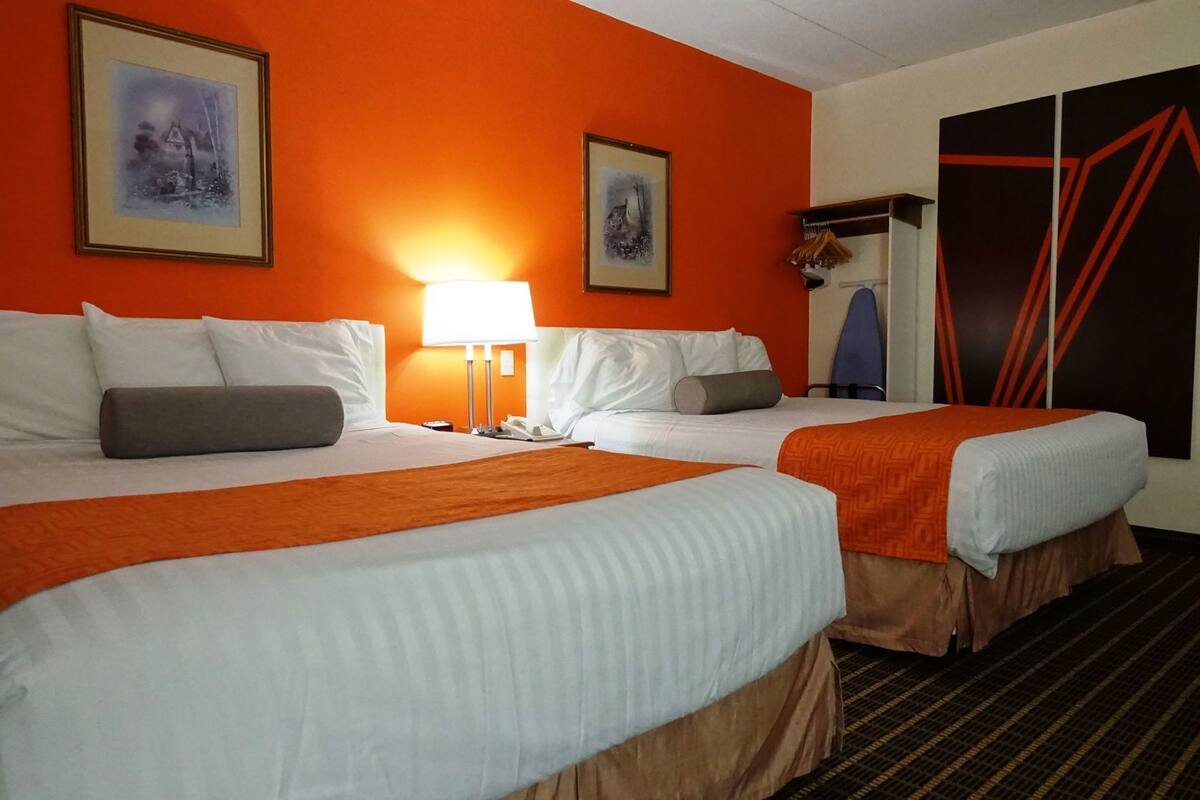 Een hotelkamer met twee bedden, een nachtkastje met een lamp en twee ingekaderde foto’s aan de muur.