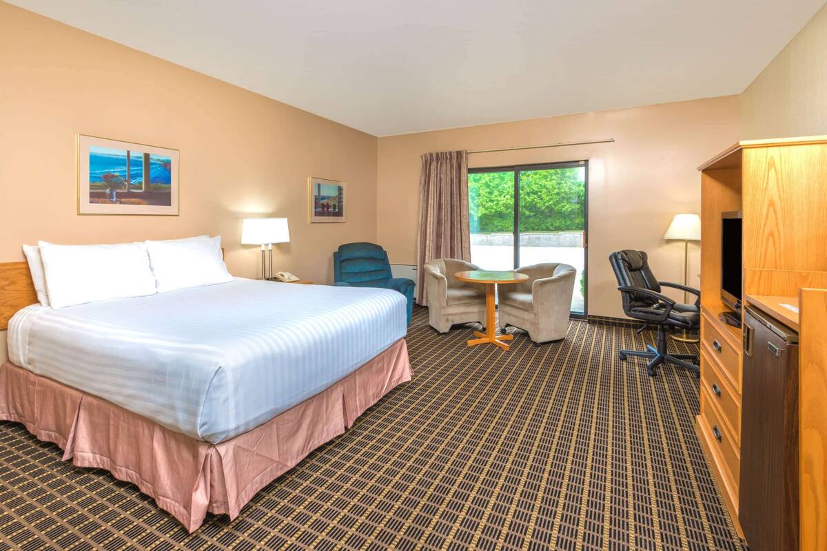 Hotelkamer met een groot bed, twee fauteuils, een tafeltje, een bureau met een televisie en een raam met gordijnen.