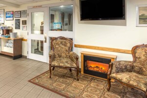 Un vestíbulo acogedor con chimenea, sillas estampadas, la entrada a una cafetería y un televisor montado en la pared.