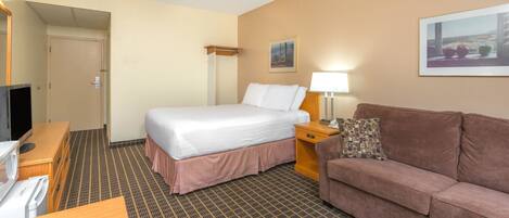 A hotel room with a bed, a couch, a TV, a desk, and a lamp.