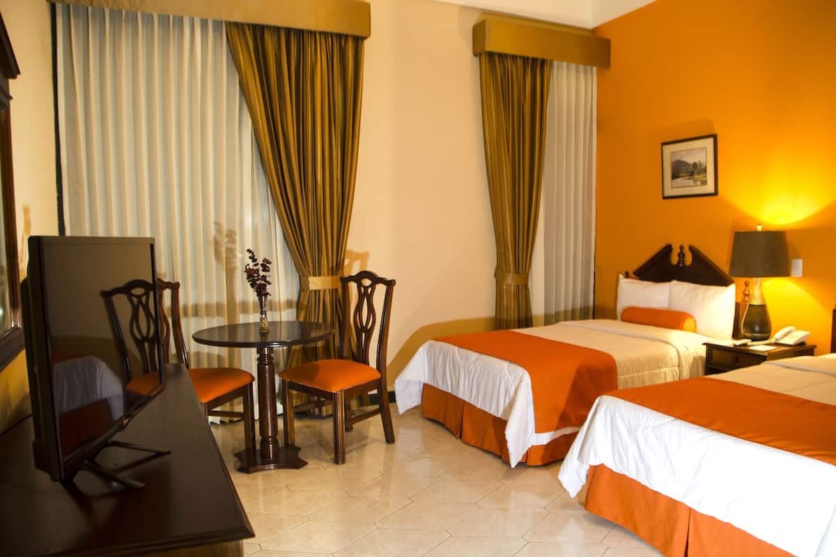 Une chambre d’hôtel avec deux lits, un bureau, une chaise, une table et une lampe.