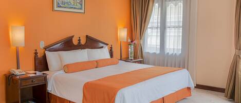 A hotel room with a large bed, two bedside tables, a nightstand, a painting on the wall, and a window with curtains.