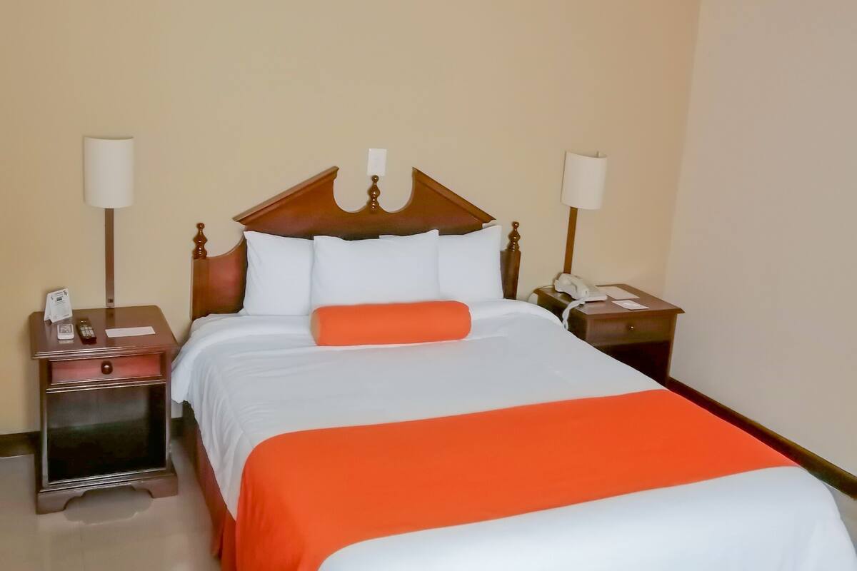 Une chambre d’hôtel avec un grand lit, deux tables de chevet, un ventilateur de plafond et une lampe fixée au mur.