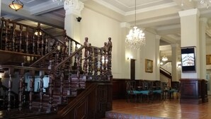 Una imponente escalera con barandales ornamentales que conduce a una zona de descanso con asientos y televisor.