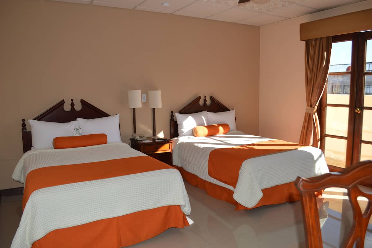 Une chambre d’hôtel avec deux lits, chacun recouvert d’une couvre-lit orange et blanche, doté d’une tête de lit en bois et agrémenté d’une table de chevet avec une lampe.