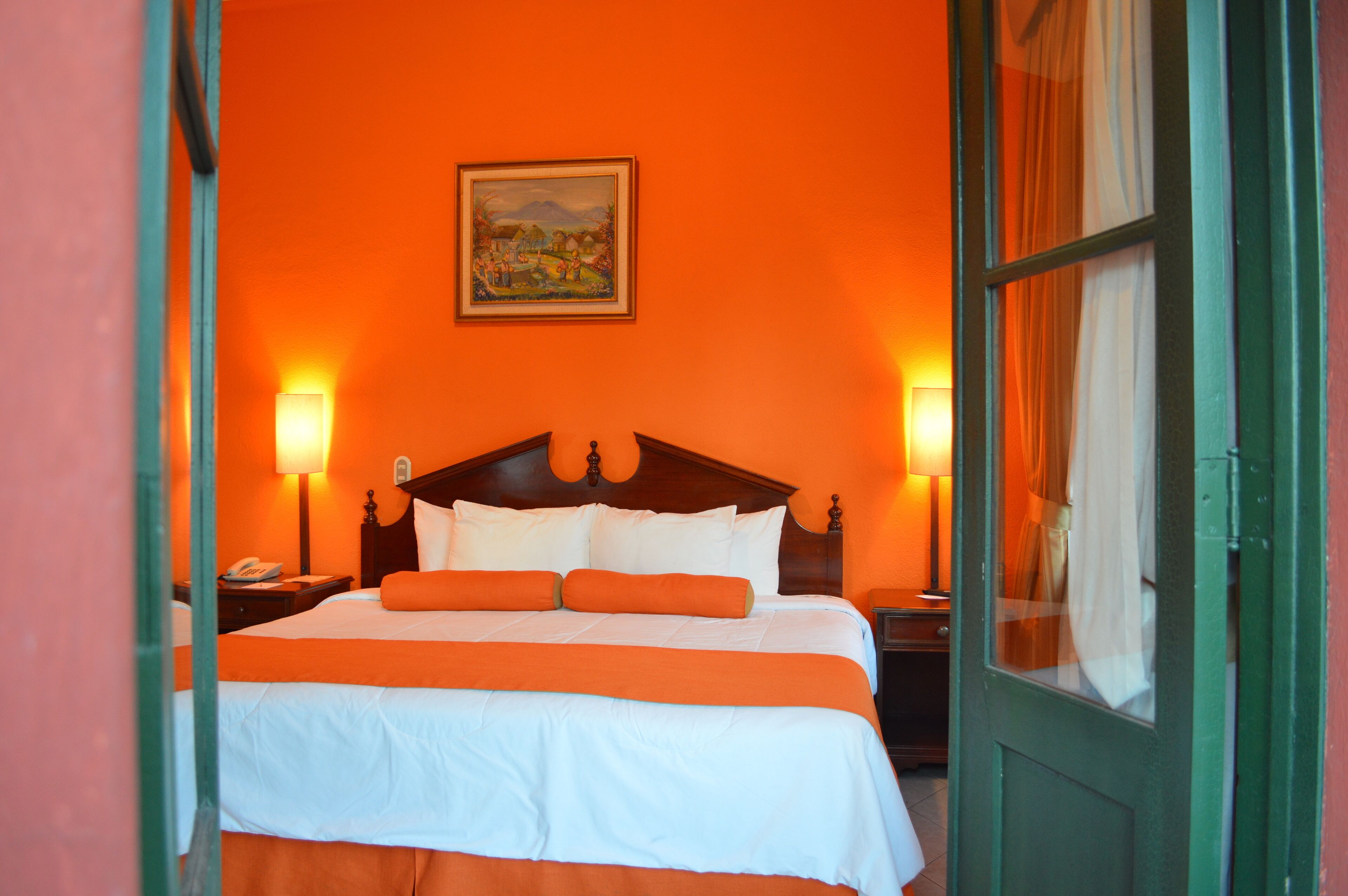 A hotel room with a large bed, two bedside lamps, a nightstand, and a painting on the wall.