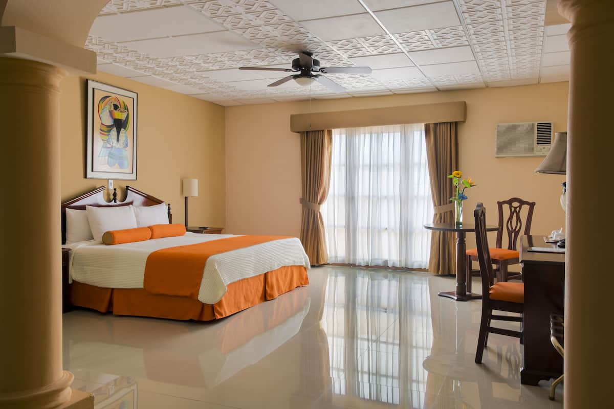 Une chambre d’hôtel équipée d’un lit, d’un bureau, d’une chaise, d’un ventilateur de plafond et d’une fenêtre avec des rideaux.