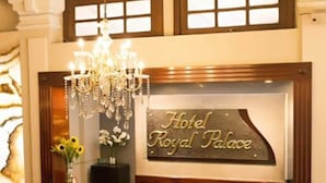 Zona de recepción con una araña, un cartel que dice "Hotel Royal Palace" y un suelo de baldosas.
