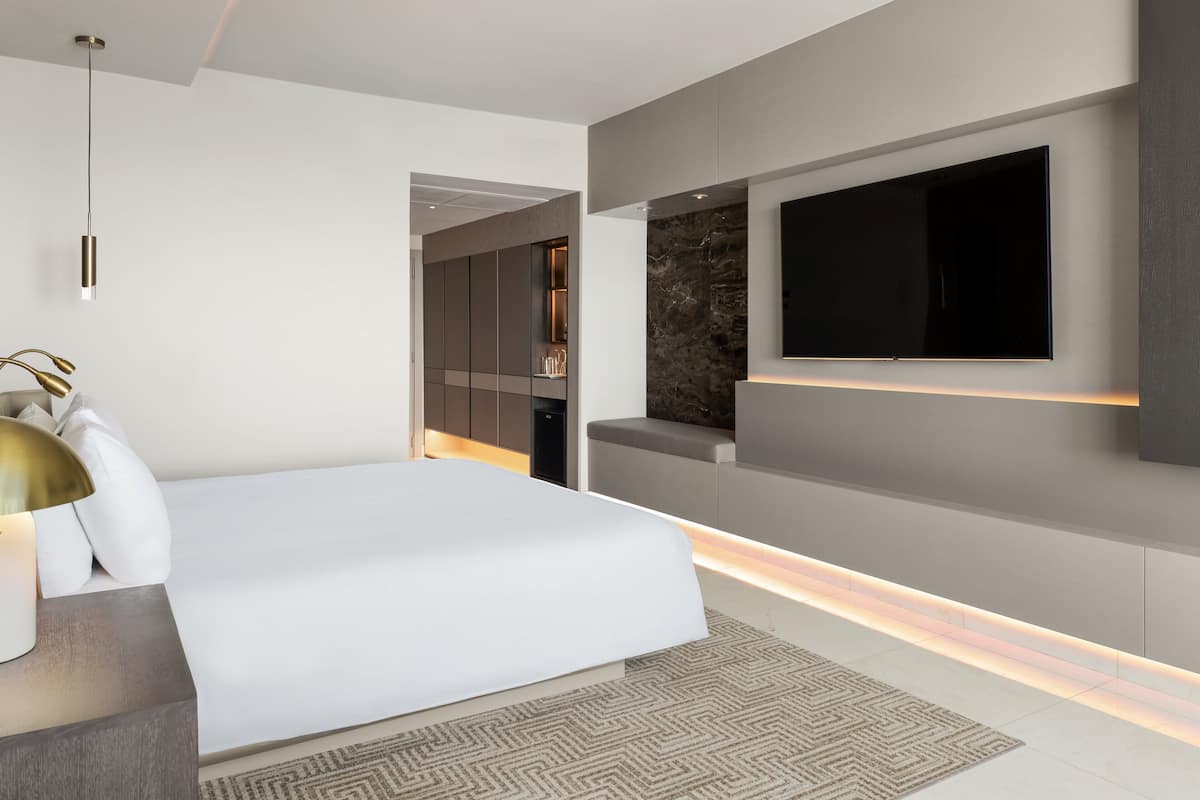 A modern bedroom with a large bed, a flat-screen TV mounted on the wall, and a built-in bench with a marble-like texture.