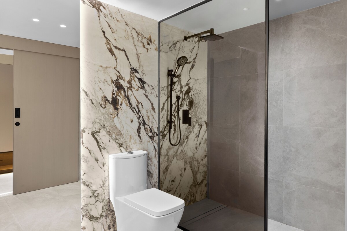 A modern bathroom with a glass-enclosed shower, a toilet, and marble walls.