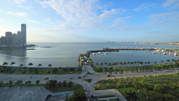 A coastal cityscape with a marina, high-rise buildings, and a road leading to a roundabout.