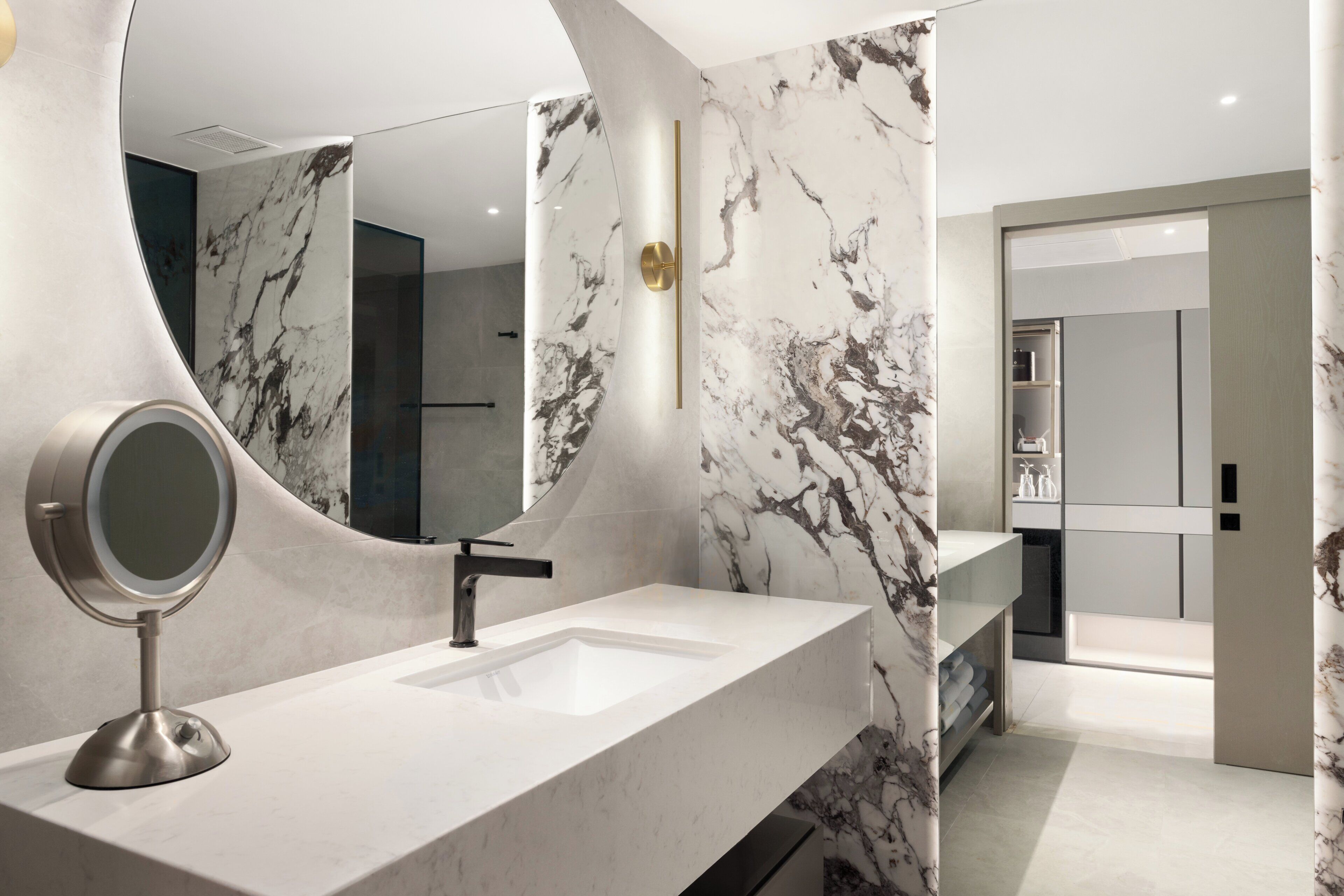 A modern bathroom with a marble vanity, a round mirror, and a sleek faucet.