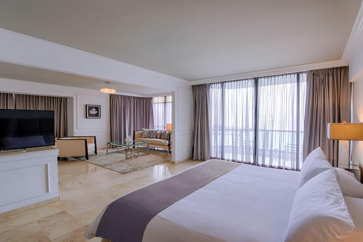 A hotel room with a large bed, a TV, a sofa, and a balcony with curtains.