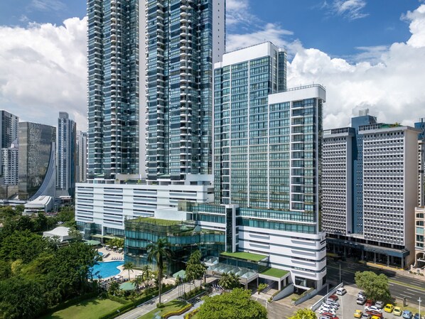 A high-rise hotel with multiple floors, a swimming pool, and a well-maintained garden area.