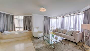 Un salón amplio con un gran ventanal, un sofá, un sillón, una mesa de centro de cristal y una bañera.